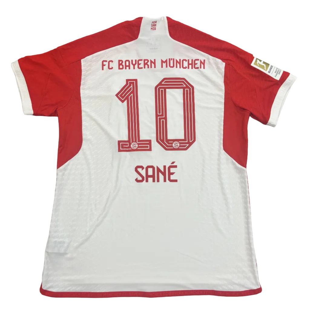 White and red sports jersey with 'FC Bayern Munich' and number '10' on a gray surface.