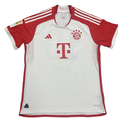 White sports jersey with red accents on a gray surface, featuring Adidas and Bayern Munich logos.